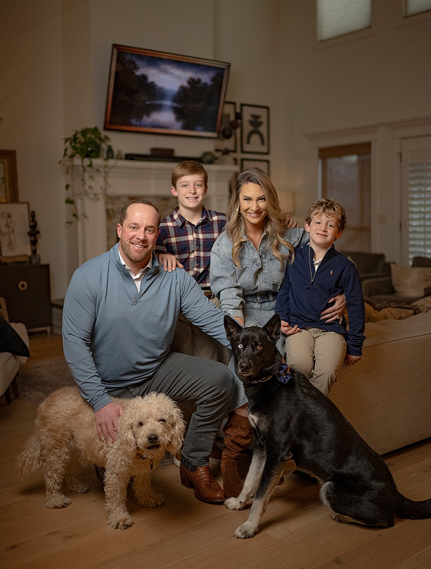 Family of four with two dogs in living room, smiling at camera.