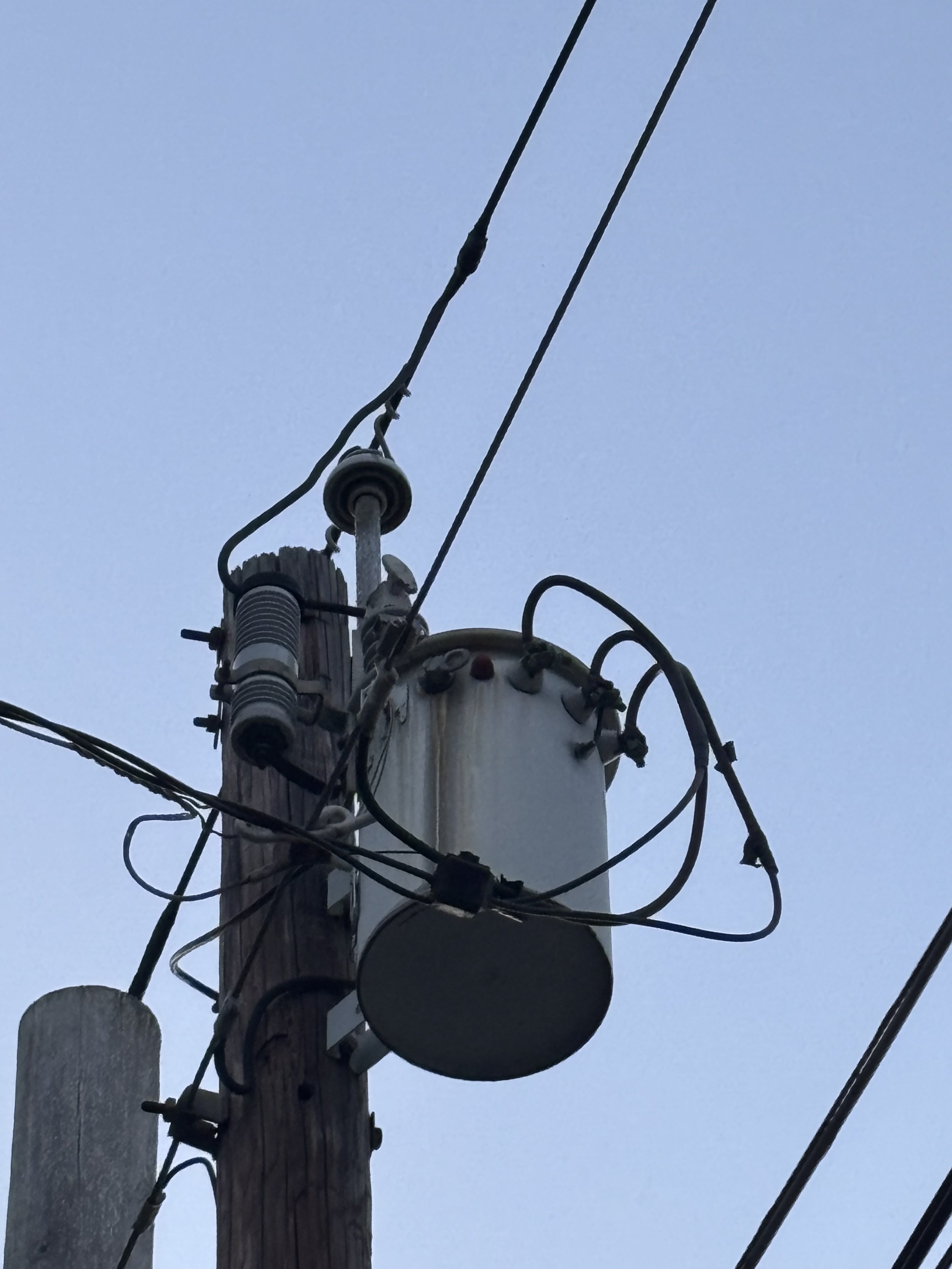 A utility pole with wires, insulators, and equipment against an overcast sky.