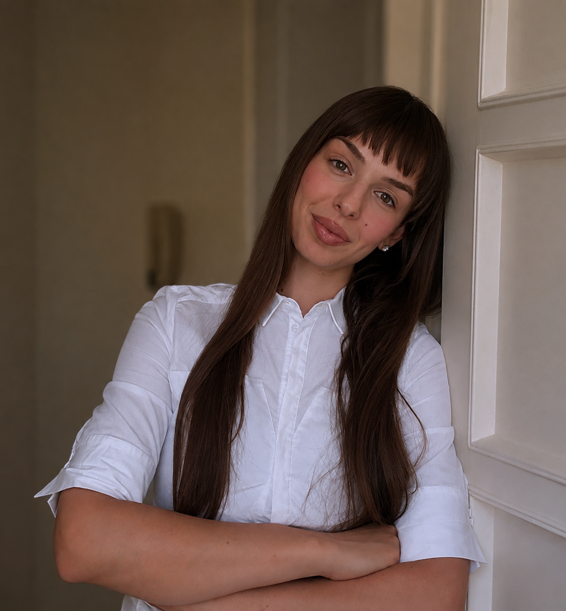 Psicologa con lunghi capelli castani, che indossa una camicia bianca, sorride e si appoggia alla porta.