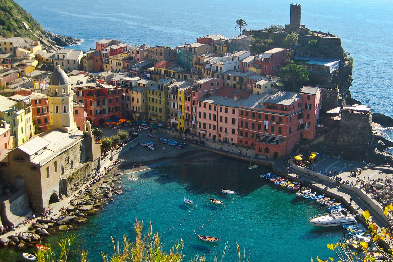 Colorful buildings surround a small harbor with boats, in a coastal village on the water's edge.