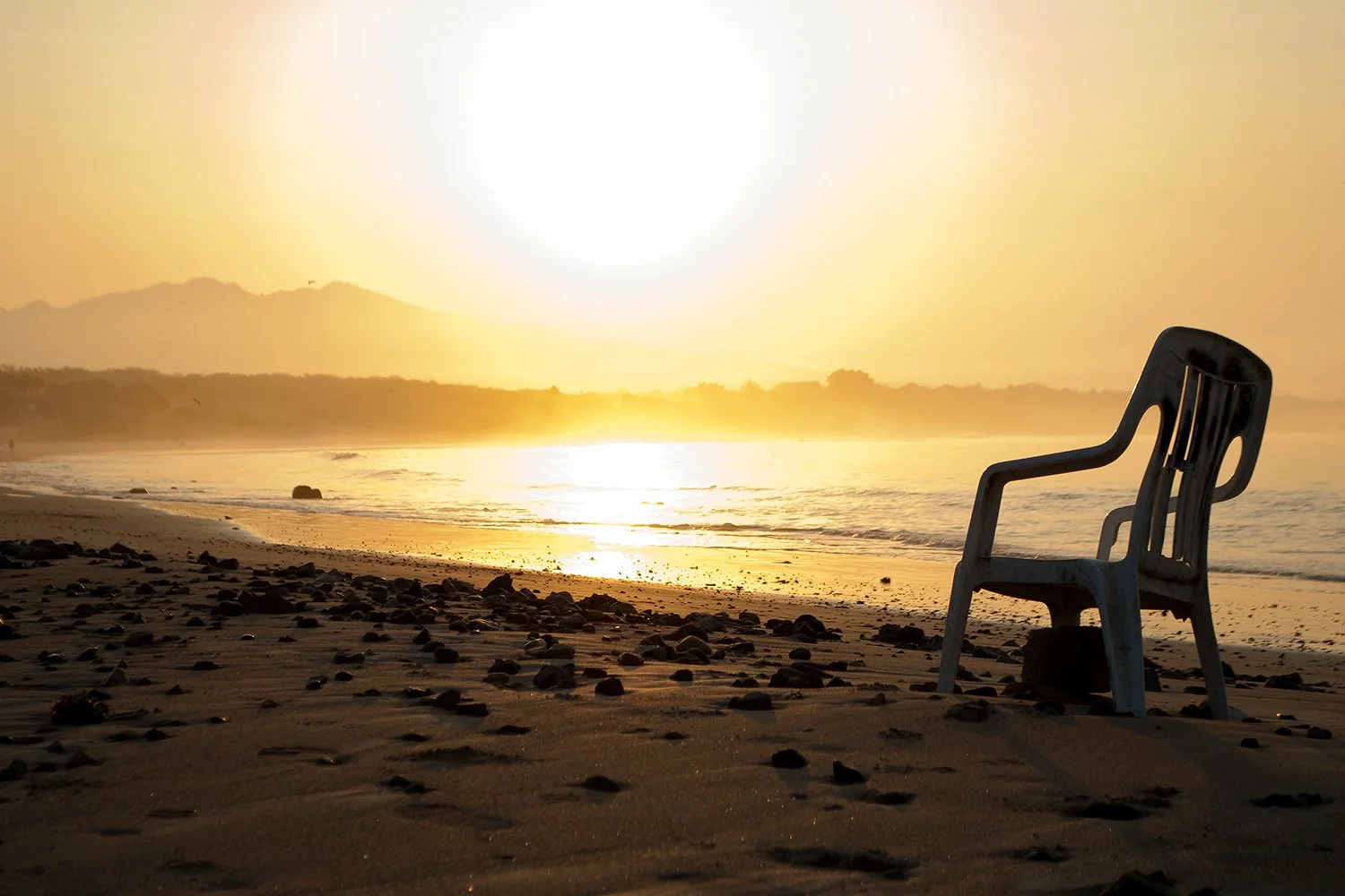 Empty plastic chair on a beach during sunset with rocks and waves