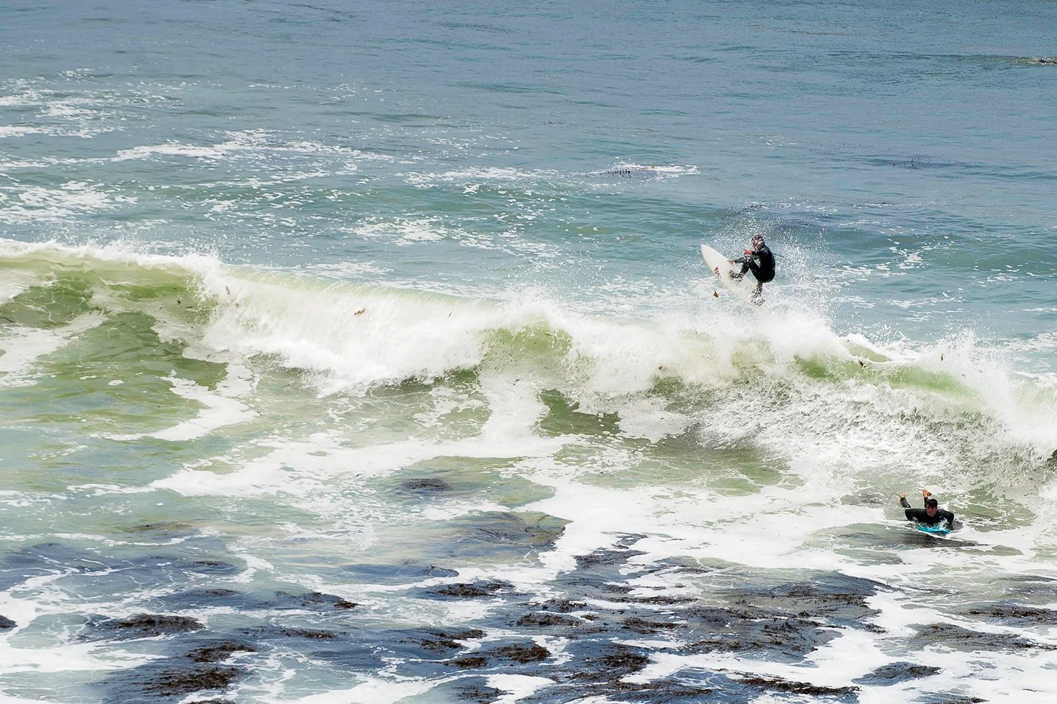 A surfer riding a wave and a person paddling on a surfboard in the ocean.