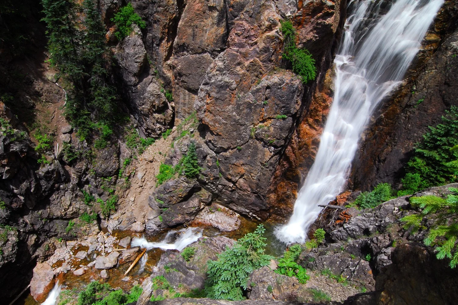 A tall waterfall cascading down rocky cliffs surrounded by green trees and plants.