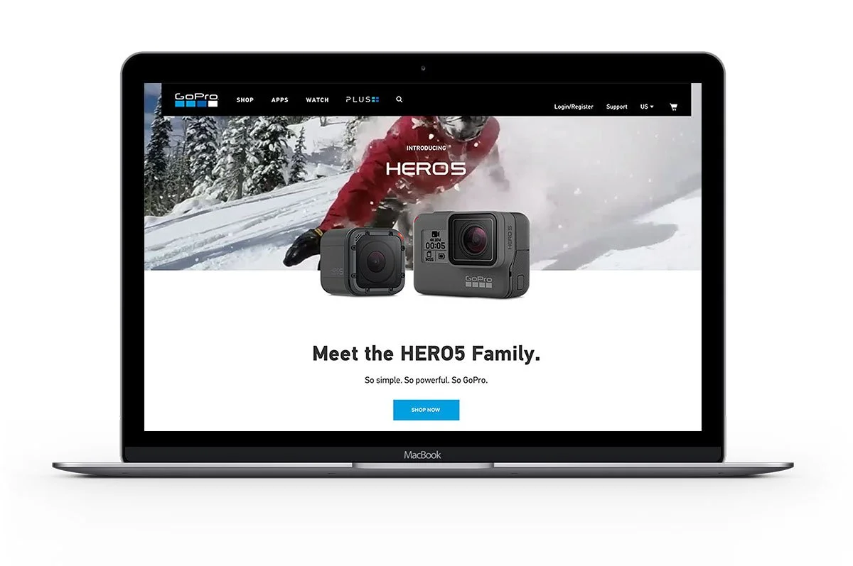 Laptop displaying a webpage for GoPro HERO5 camera, featuring a snowy mountain outdoor scene and two HERO5 action cameras, with a person snowboarding in the background.