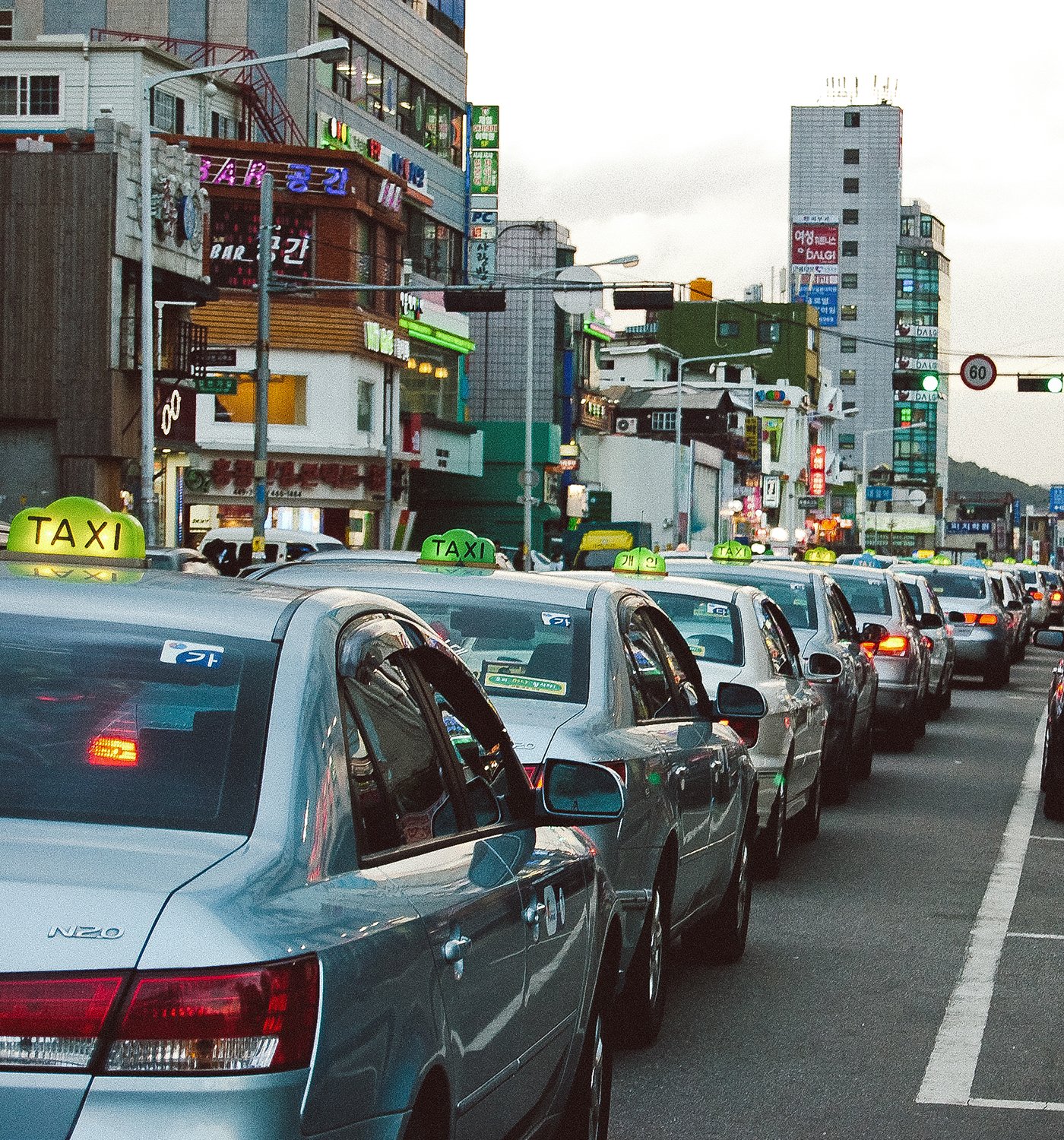 Traffic jam with multiple silver taxis on a busy city street in South Korea, buildings with colorful signs in the background.