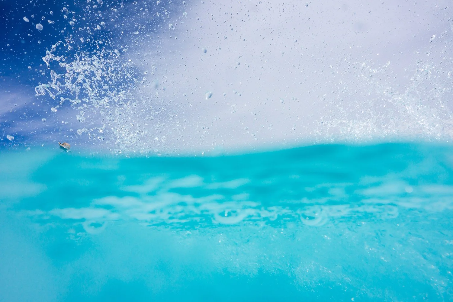 A splash of water with droplets in mid-air above a blue ocean surface on a partly cloudy sky