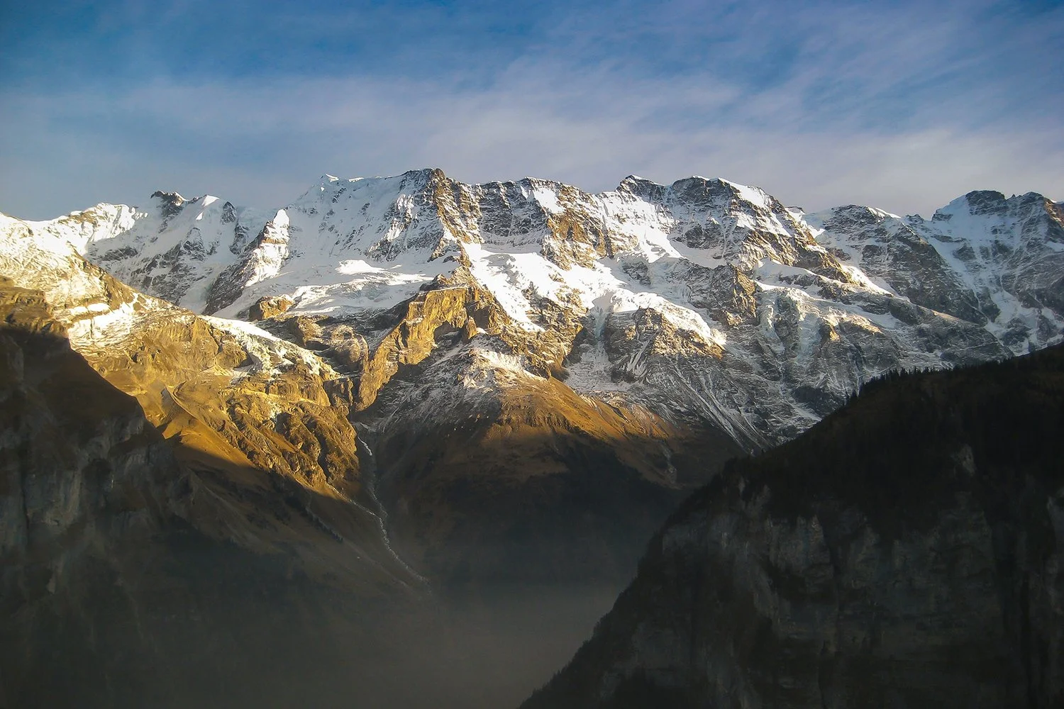 Snow-capped mountains with rugged, rocky slopes and a cloudy sky.