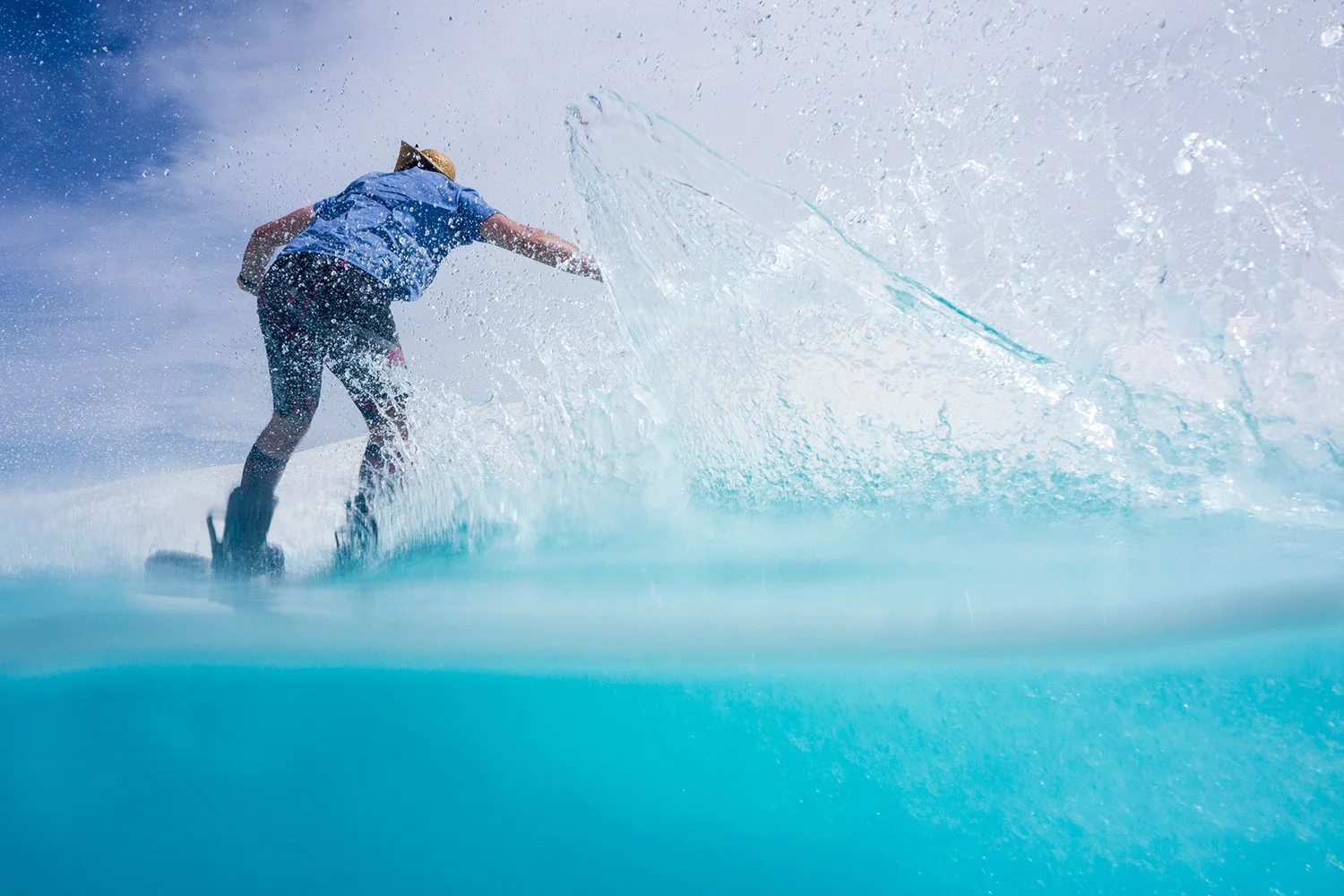 Person wakesurfing on a lake or ocean, creating a large spray of water.