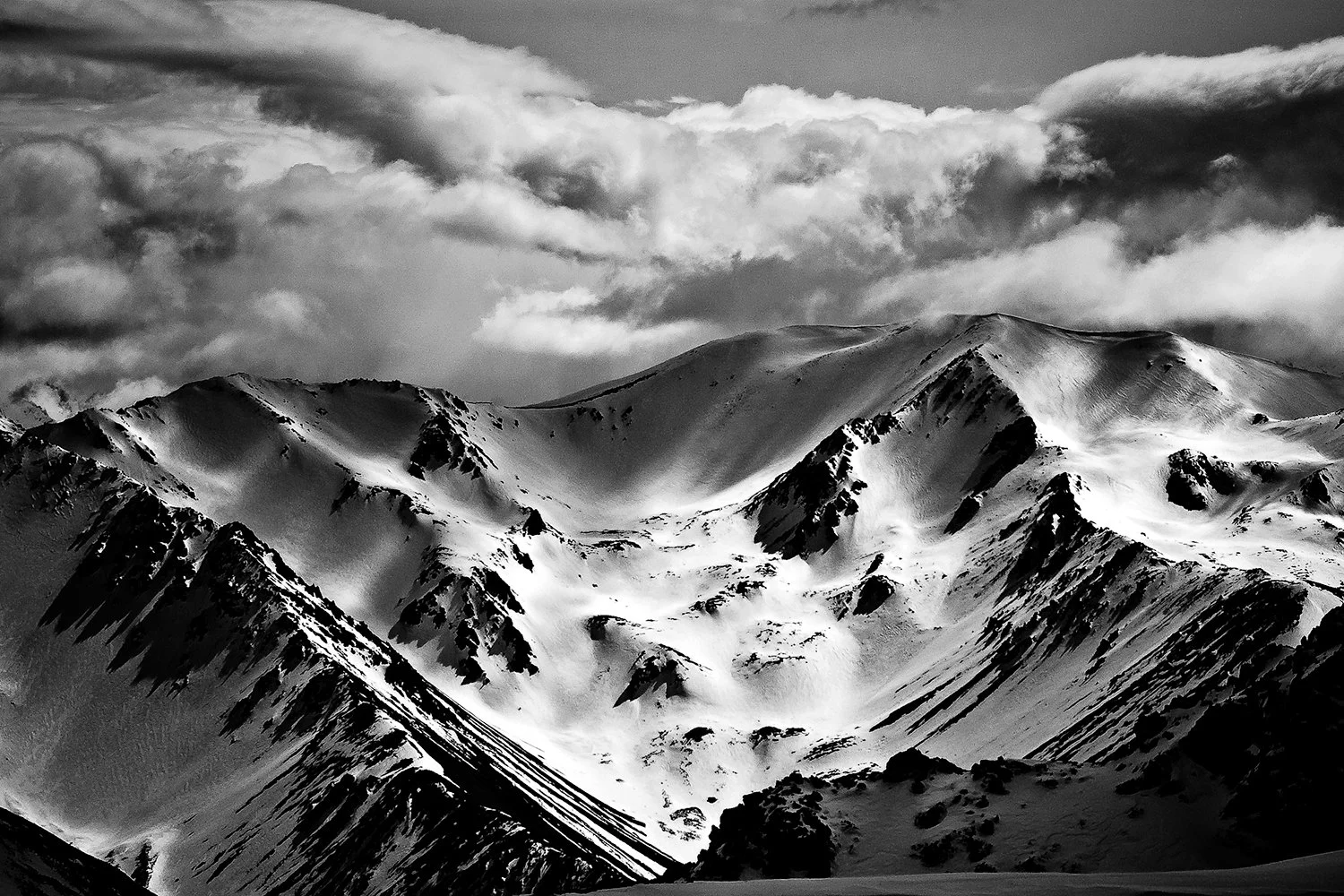 Snow-covered mountain range under a cloudy sky in black and white.