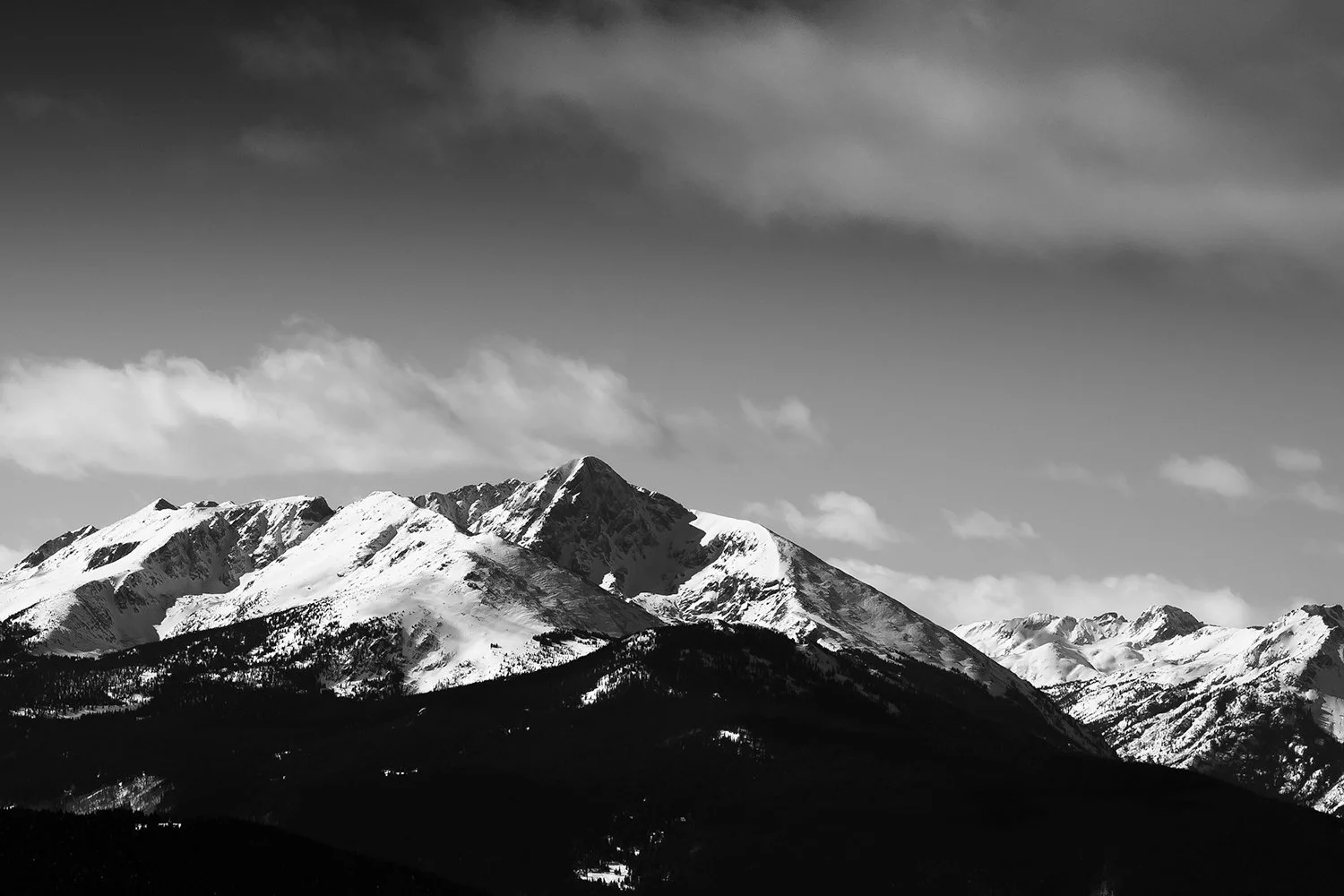 A black and white photograph of snow-capped mountains under a partly cloudy sky.