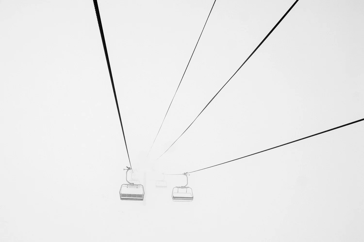 Ski lift chairs on cables disappearing into foggy white sky.