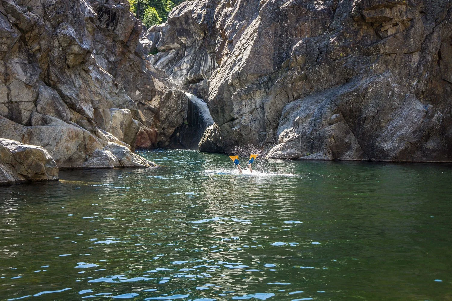 A person underwater in a river with large rocks and a small waterfall in the background.