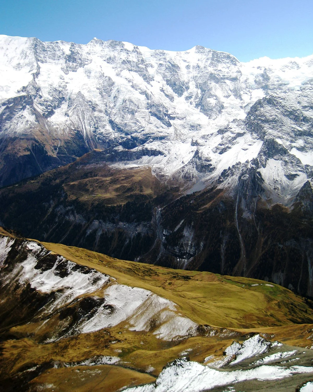 Snow-capped mountain range with rugged slopes and green valleys in the foreground.