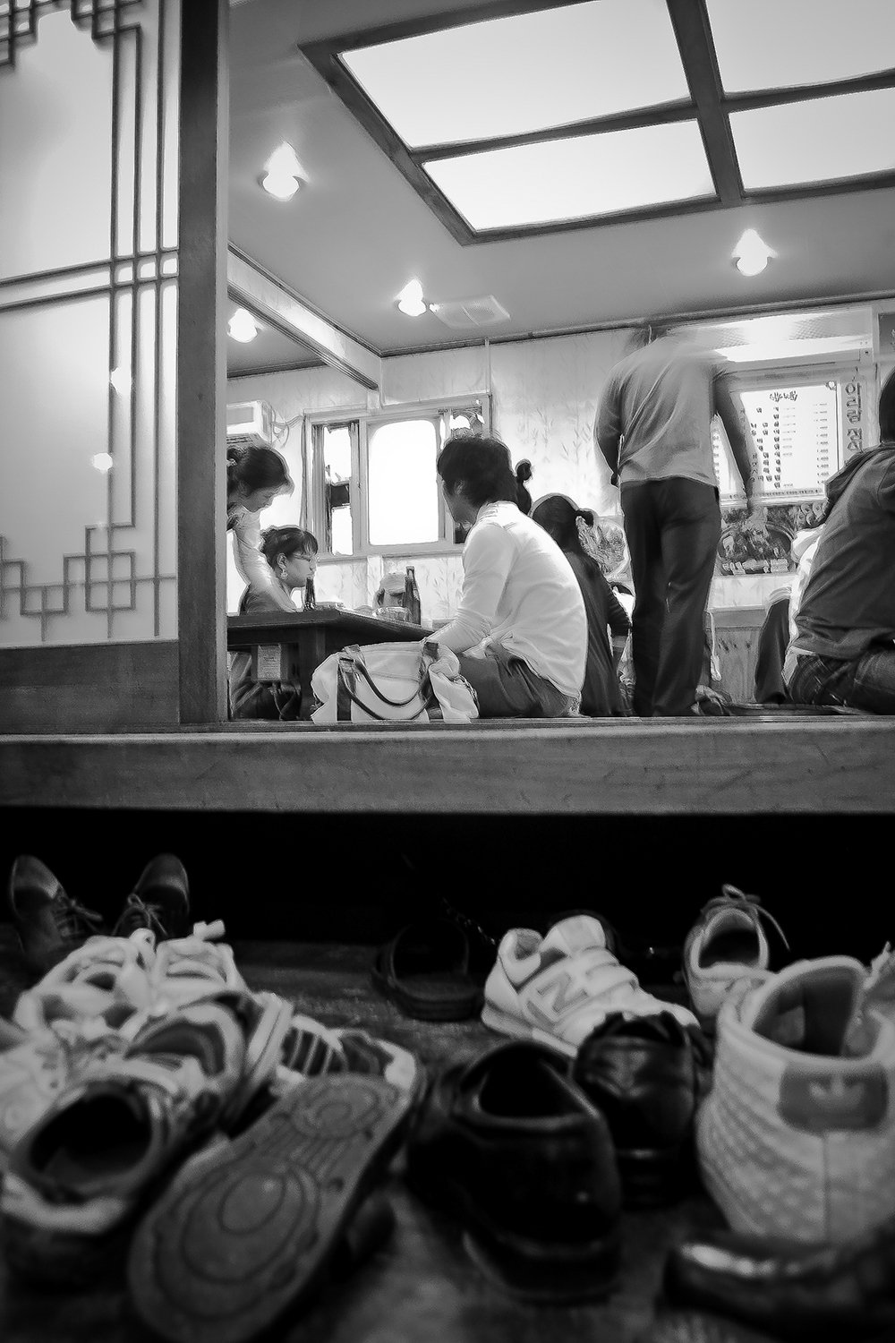 View of a restaurant from the floor with shoes lined up at the front, looking into a dining area with several people sitting and engaging in conversations.