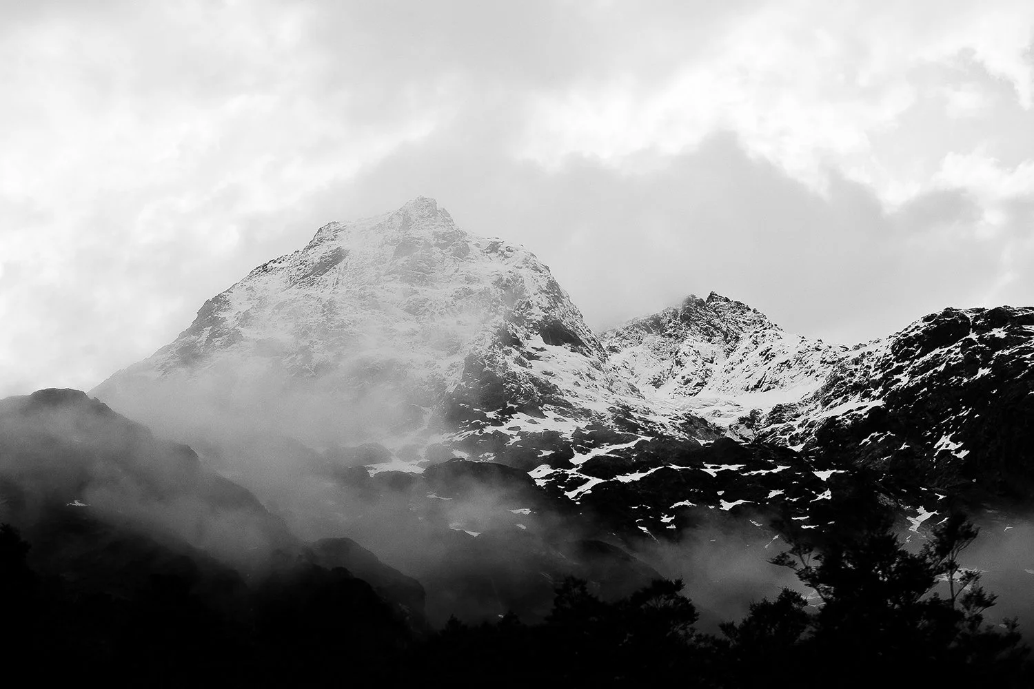 Snow-covered mountain peaks with mist and clouds surrounding the mountainous landscape in black and white.
