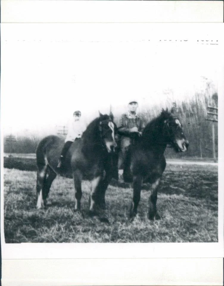 Two boys sitting on horseback in an open field, with trees and power lines in the background, appears to be an old black-and-white photo.