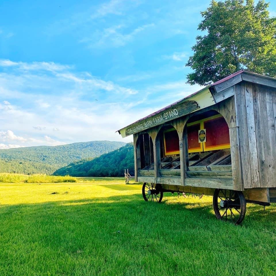 An old wooden barn on wheels situated in a lush green field with mountains in the background and a bright blue sky.