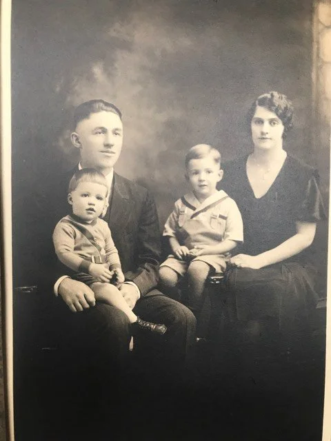 Black and white photo of a family portrait with a man, woman, and two young boys, all dressed in vintage clothing.