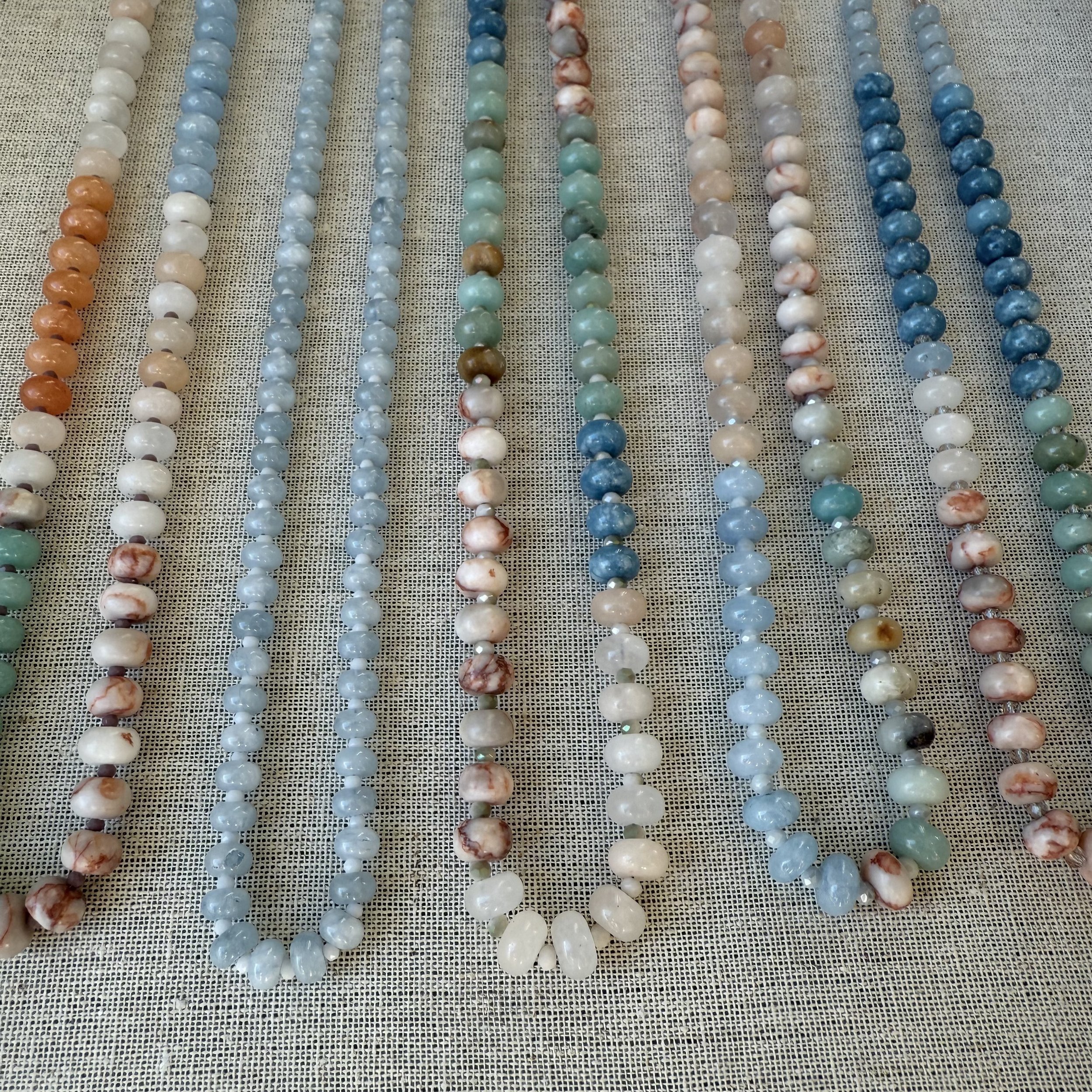 Various strands of colorful beads made of shells, arranged in parallel on a textured fabric background.