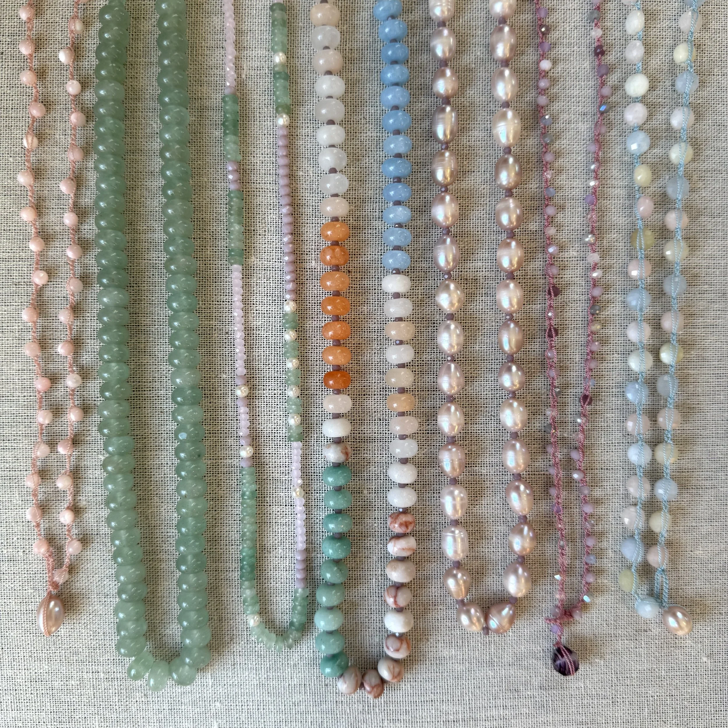 Various strands of pearl and beaded necklaces arranged vertically on a textured fabric background.