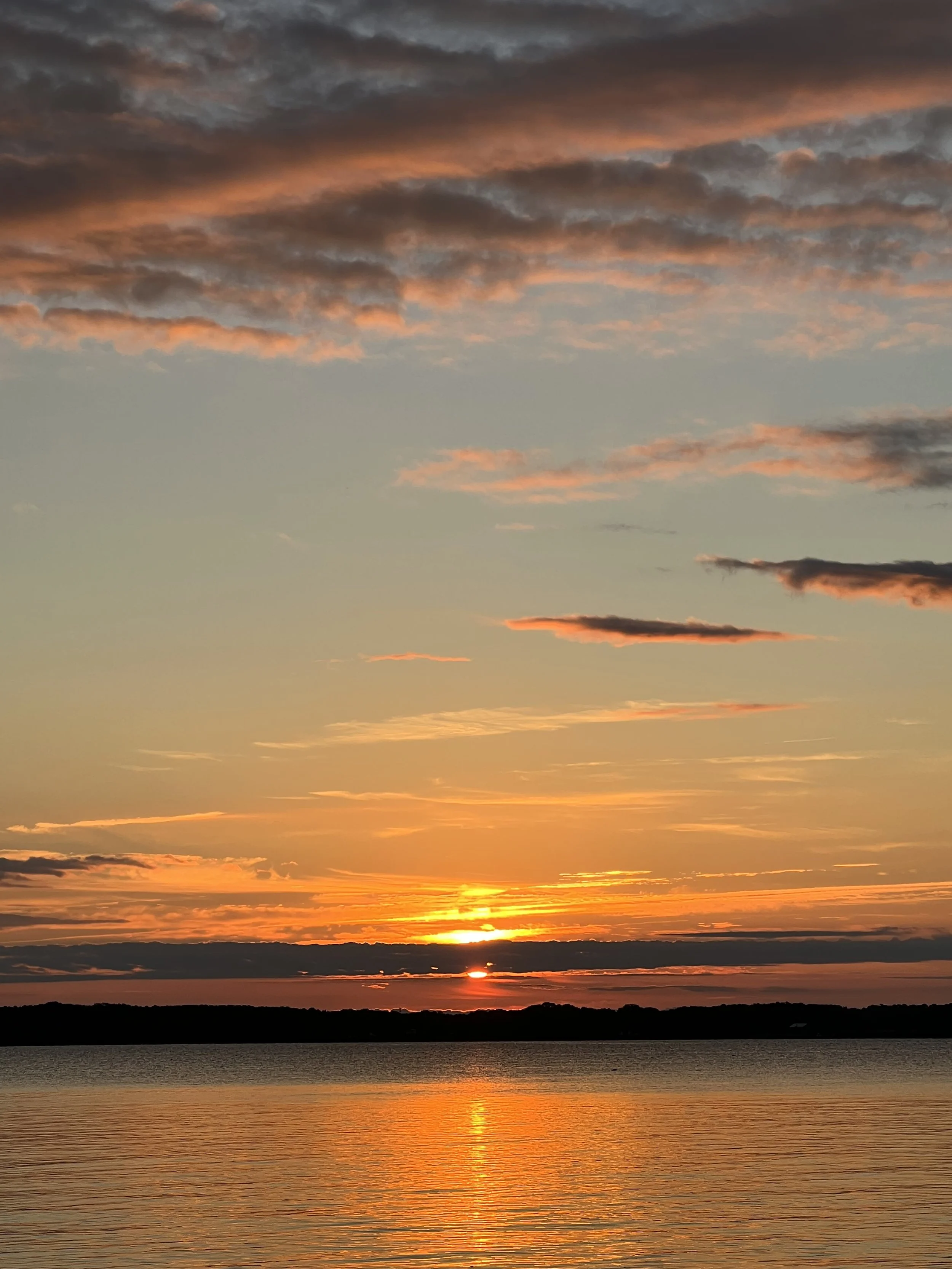 Sunset over a body of water with clouds in the sky illuminated by the setting sun.