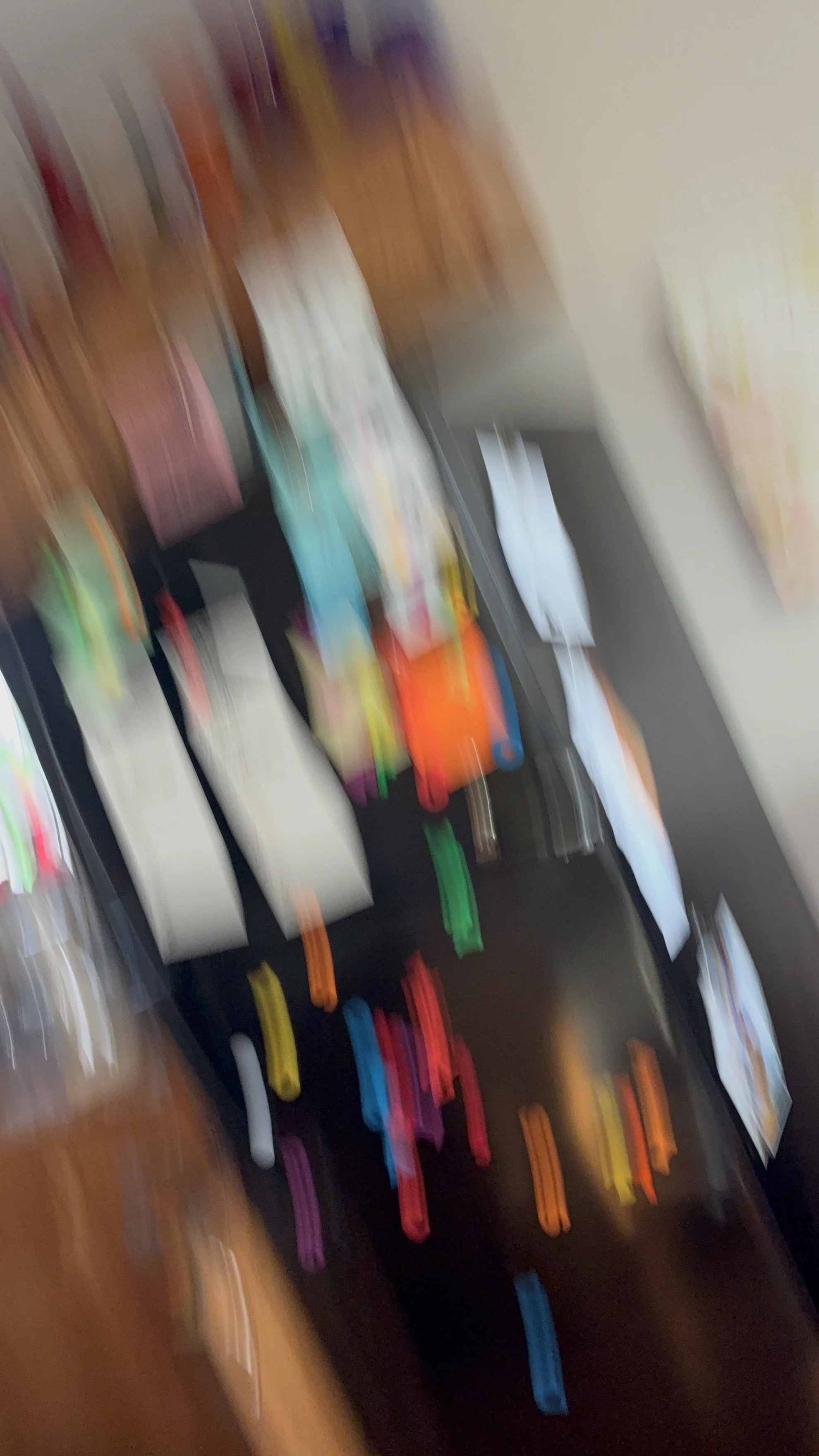 Blurry image showing various colorful objects and stationery items arranged on a surface.