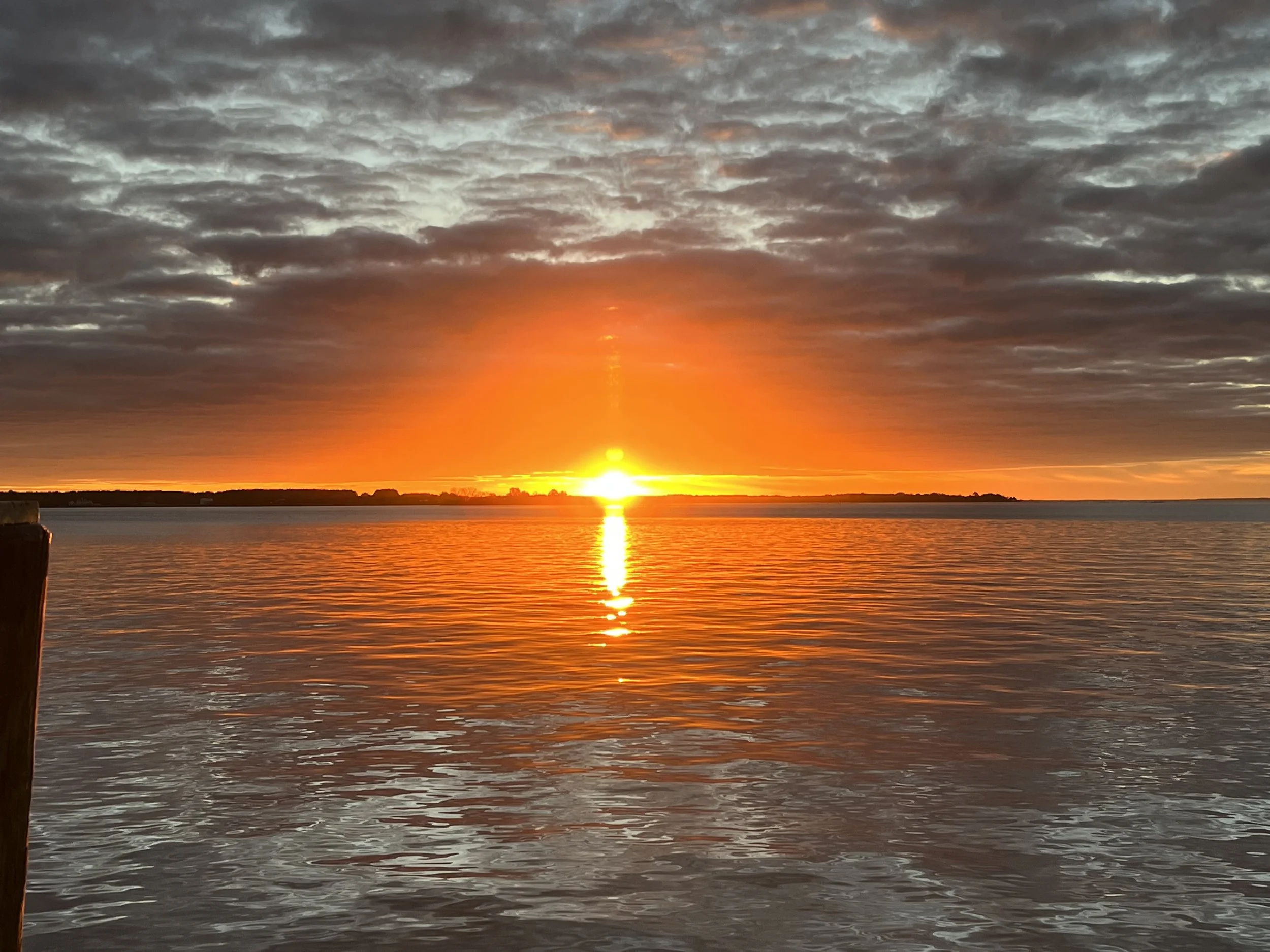 Sunset over water with partly cloudy sky and orange glow at horizon.