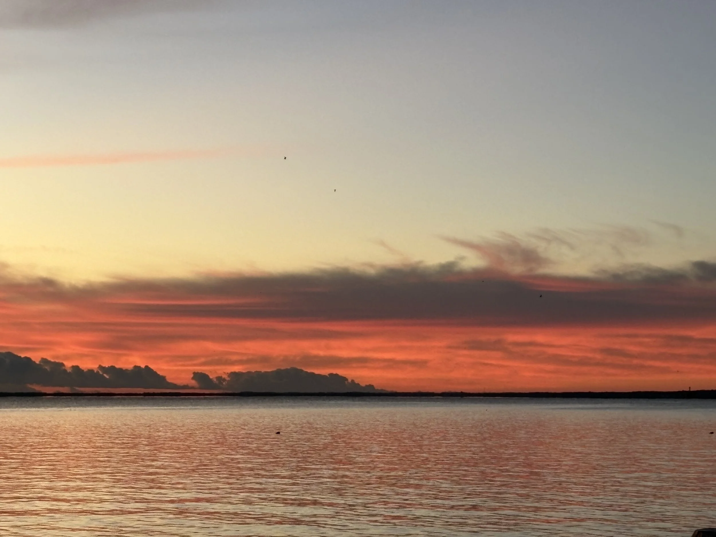 A sunset over a body of water with a mostly cloudy sky and orange, pink, and purple hues.