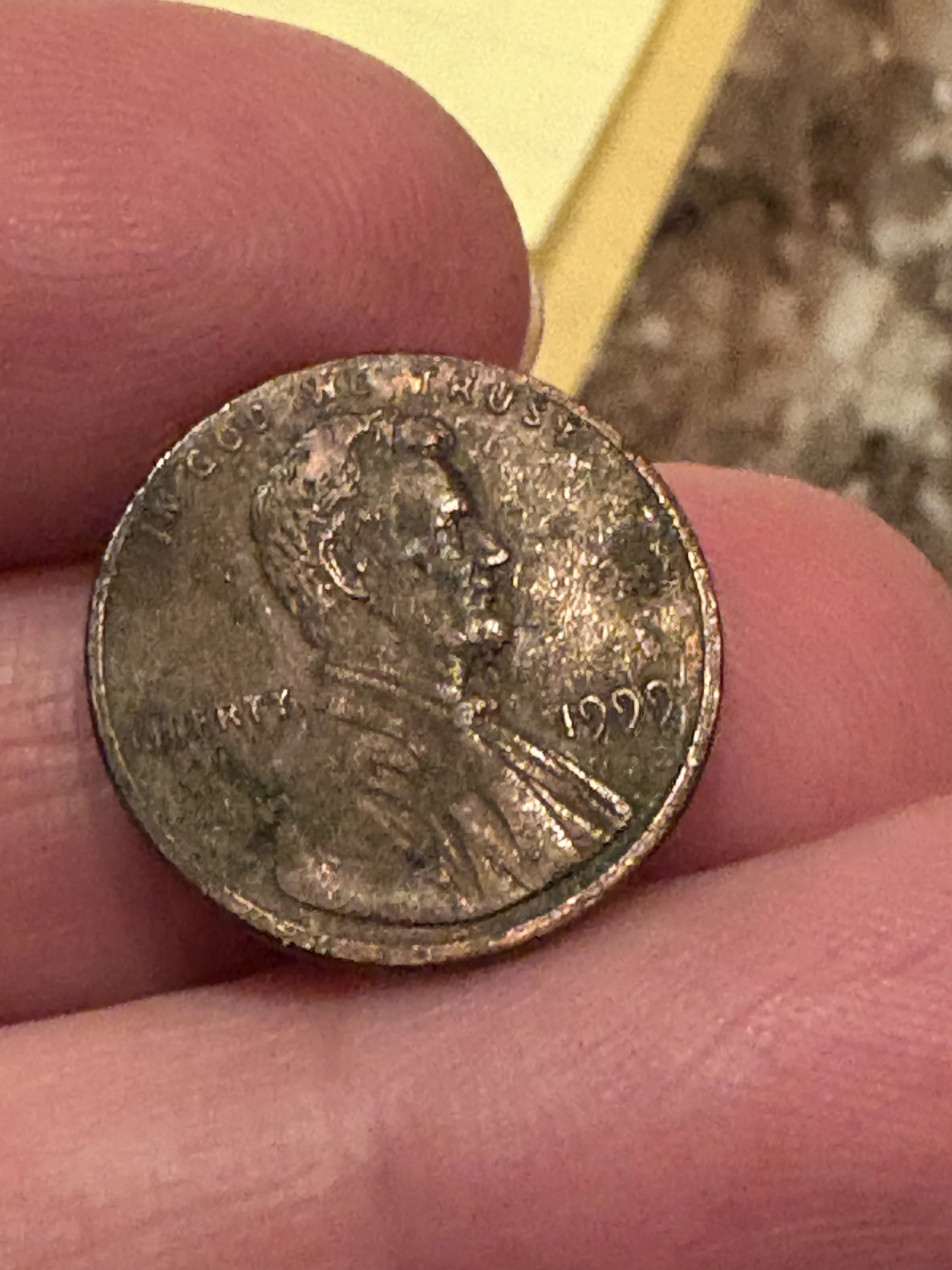 Close-up of a U.S. quarter held between fingers with pink skin, with a yellow object and blurred background.