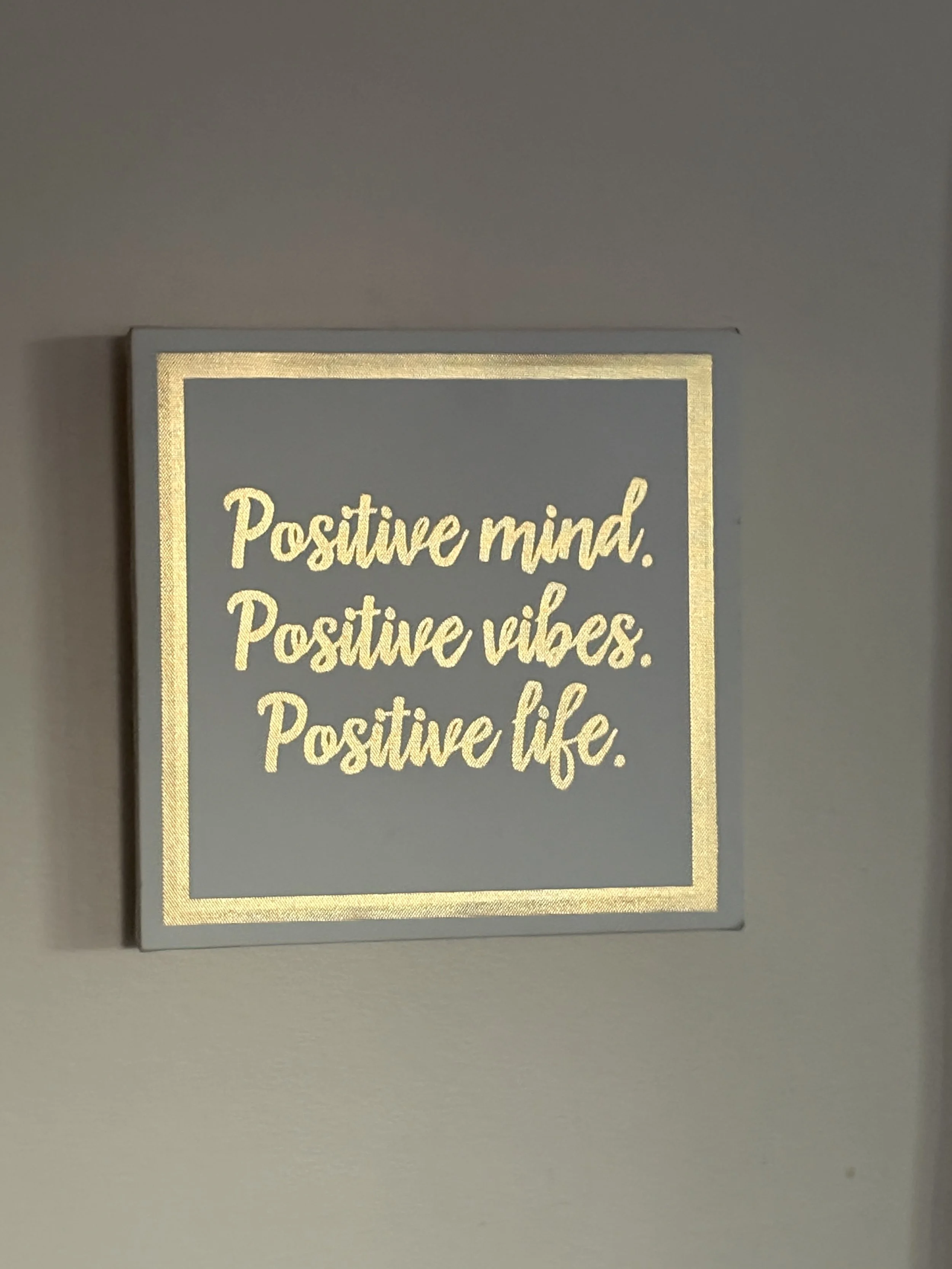 A framed quote on a grey background that reads: 'Positive mind. Positive vibes. Positive life.' in yellow lettering.