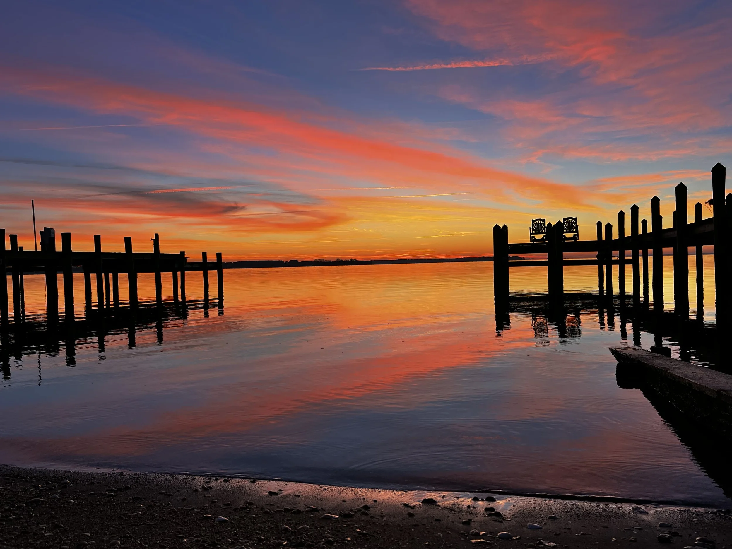A colorful sunset over a body of water with a silhouetted pier and chairs.