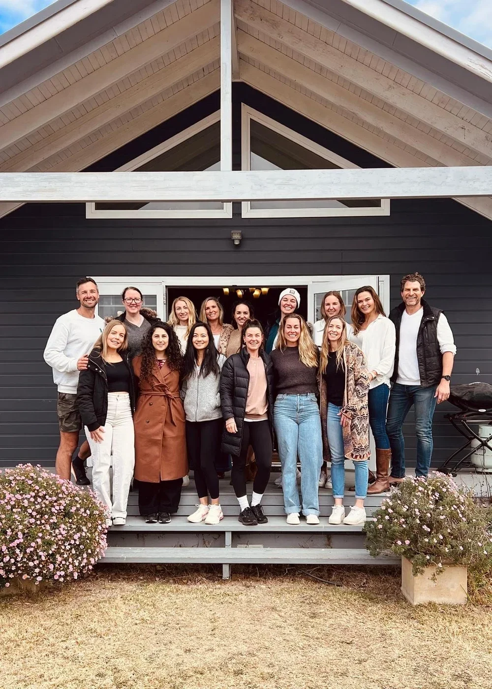 A group of adults standing on the porch of a modern house, smiling for the camera.