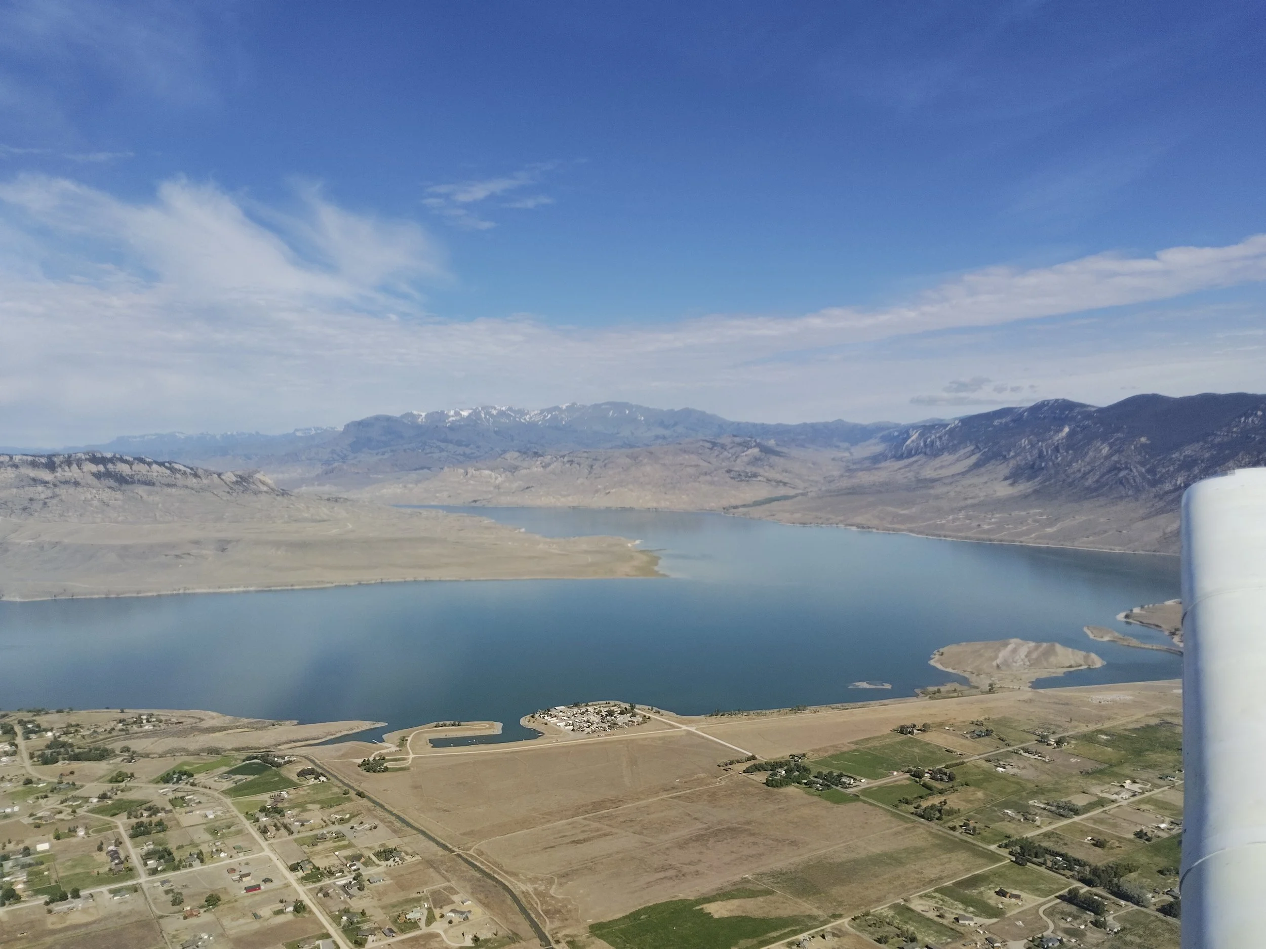 Aerial view of a landscape with a large body of water, mountains in the background, and a small residential area with roads in the foreground.