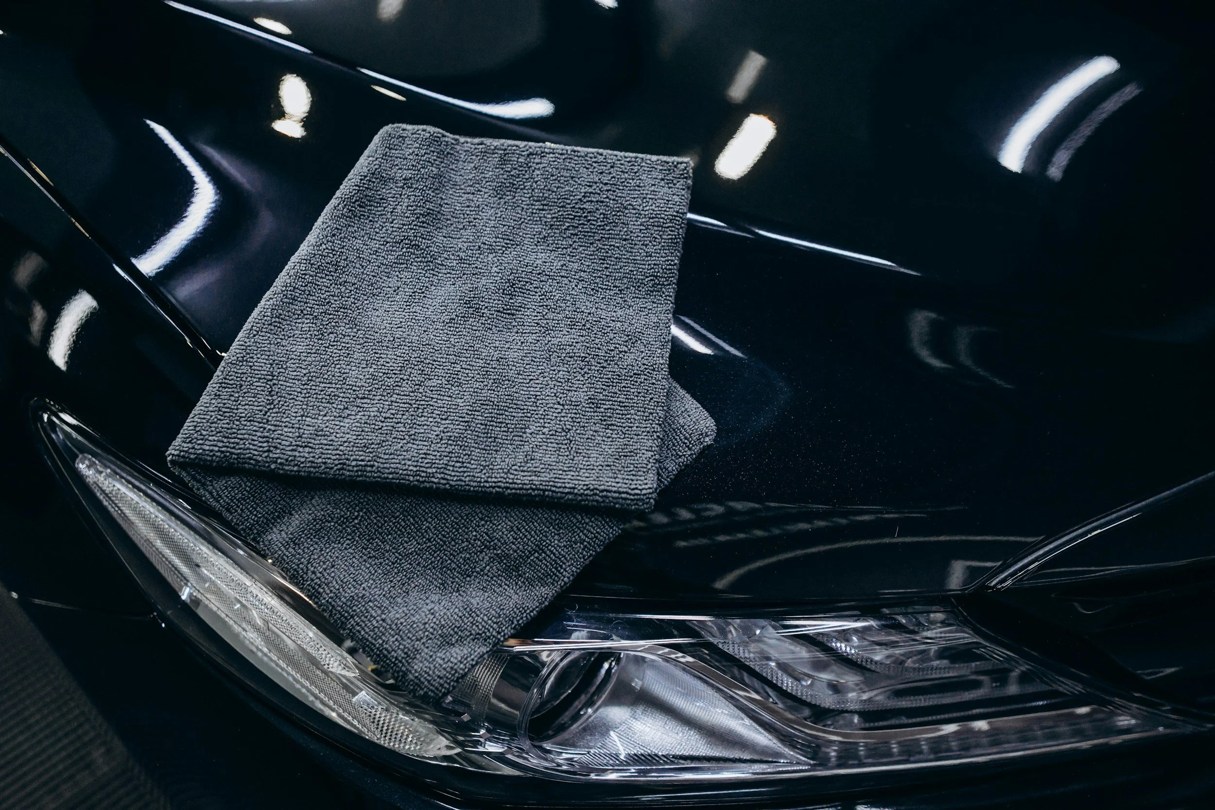Close-up of a black car's headlight with a gray cleaning cloth draped over the top of the headlight.