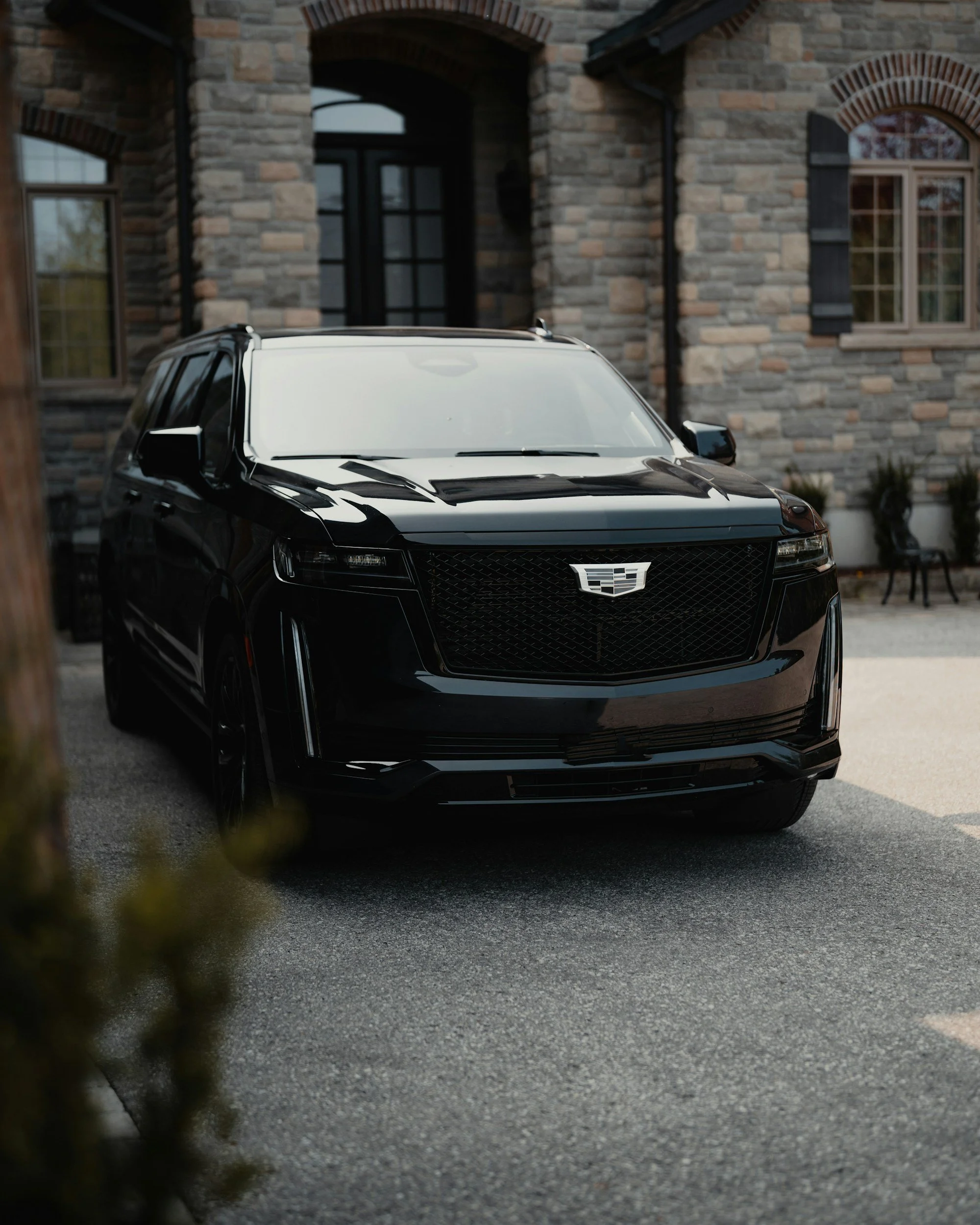 Black SUV parked in front of a stone house with arched windows and a black door.