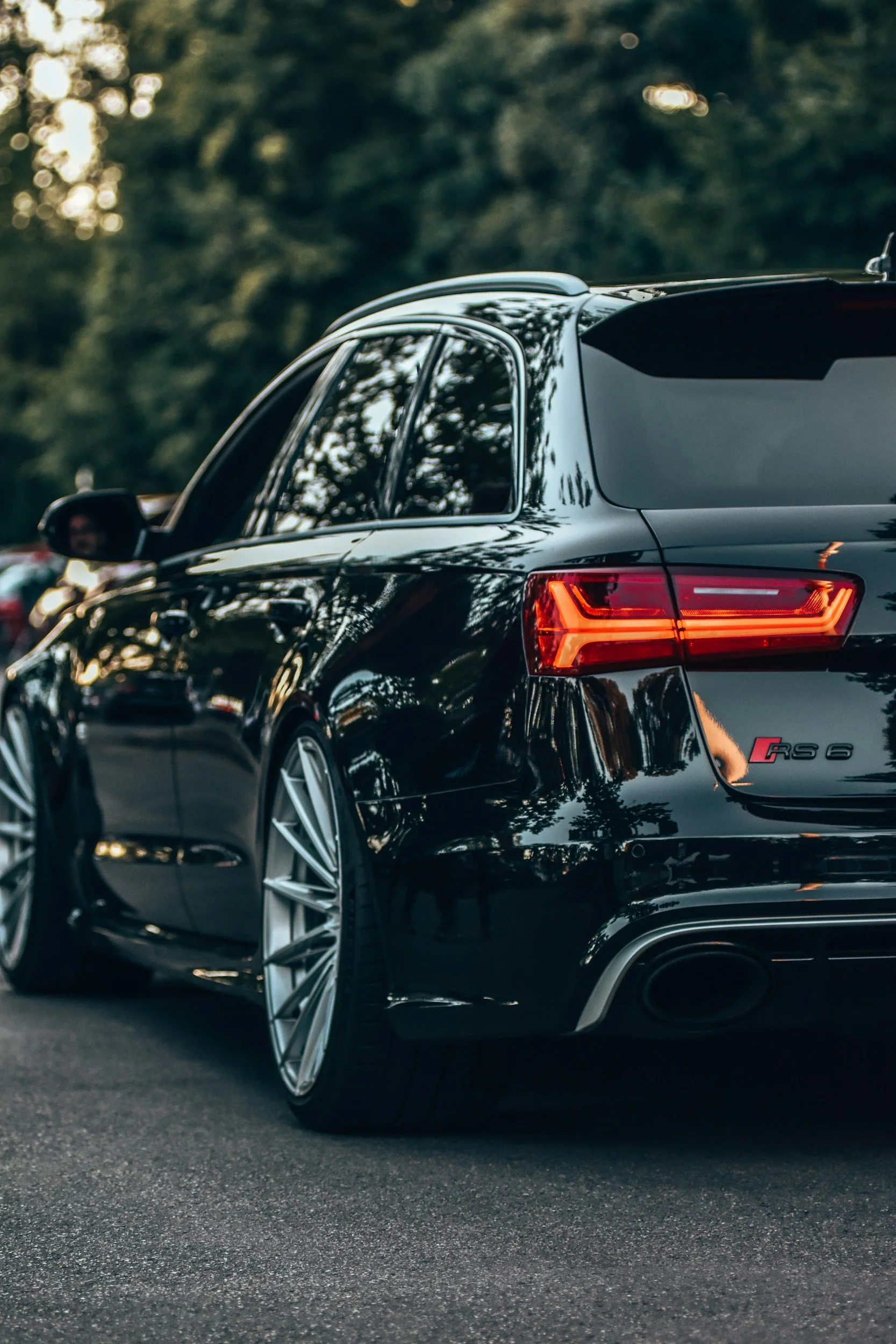 Rear side of a black Audi RS 6 station wagon parked on the street with trees and other cars in the background.