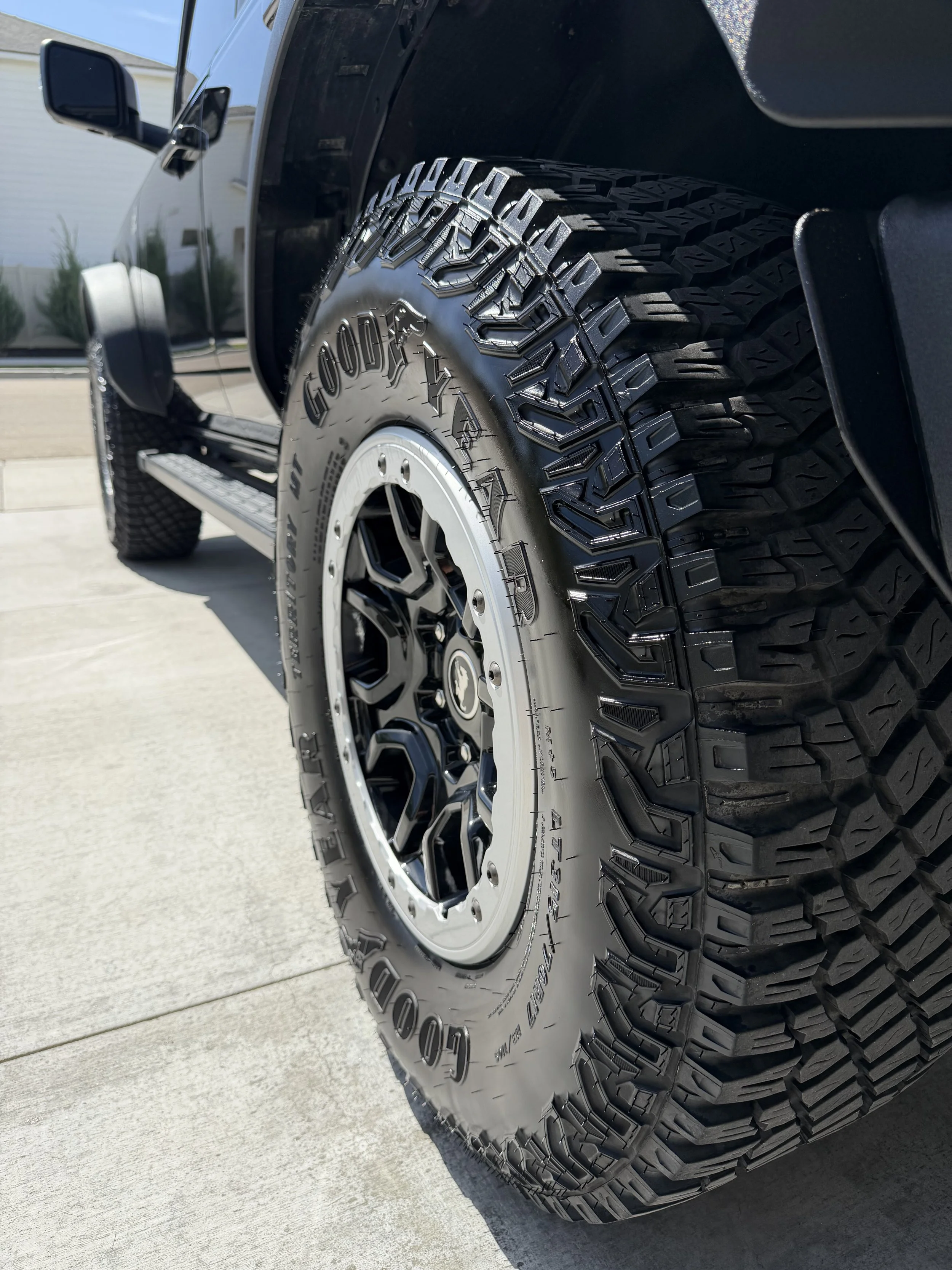 Close-up of a rugged, off-road tire on a black vehicle, showing detailed tread pattern and sidewall branding.