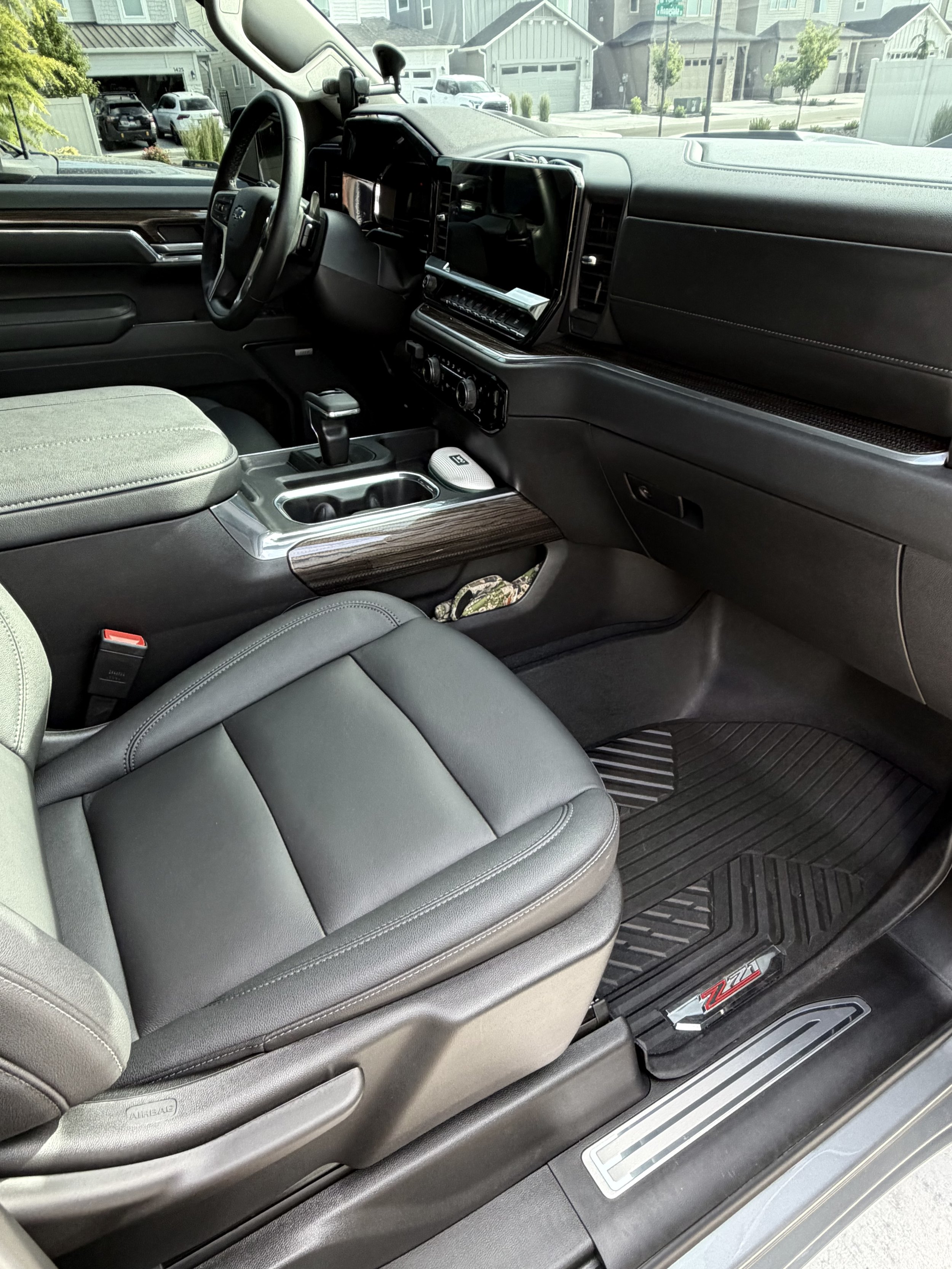 The image shows the interior of a Chevrolet Silverado Z71 pickup truck, focusing on the driver's seat, center console, dashboard, and part of the passenger seat. The interior features black leather and wood accents, with visible gear shift, cup holders, and climate controls.