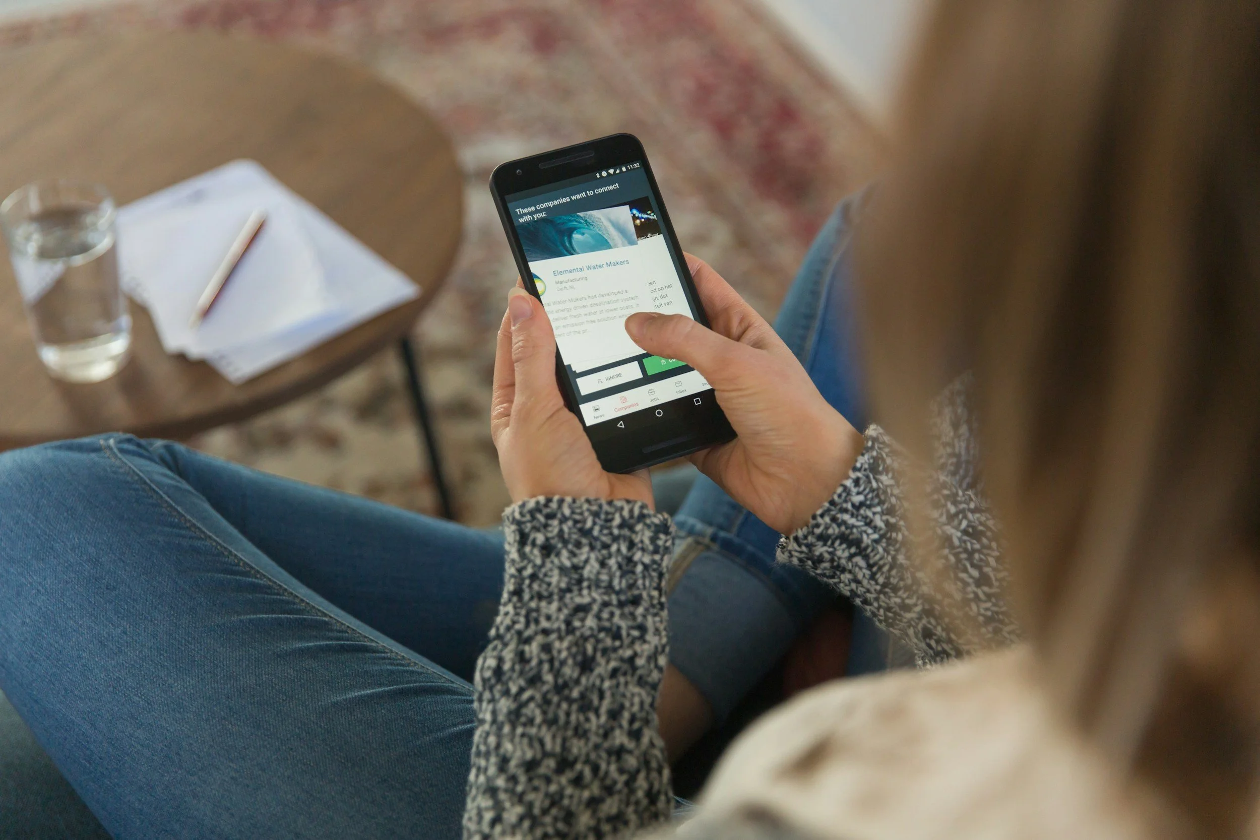 Person sitting on a chair or couch, using a smartphone. The phone displays a list of companies wanting to connect, with the company name "Elemental Water Makers" visible.