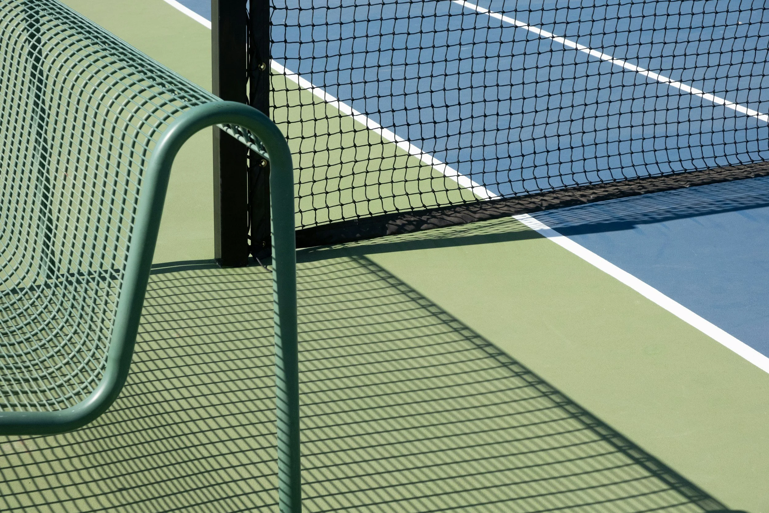 zoomed in shot of tennis court with black net and green bench