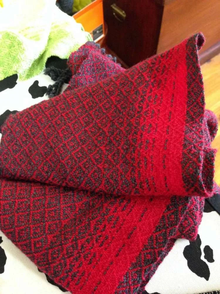 Red and black patterned woven textile item, possibly a scarf or towel, placed on a surface with a black and white cow print cloth underneath.