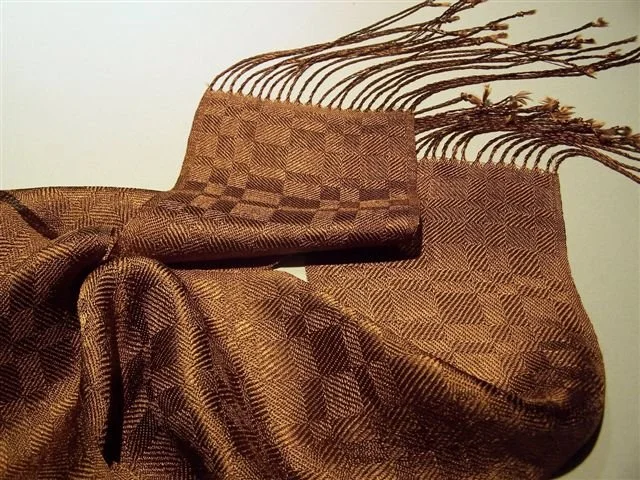 A woven textile with a checkered pattern draped over an armchair, with dried branches or twigs arranged behind it.