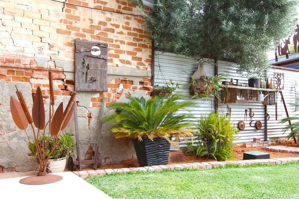 Backyard with brick and metal wall, potted plants, garden tools, and outdoor decor.