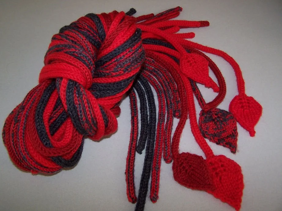 A multicolored, knitted scarf with red and black pattern featuring leaves and pom-poms.