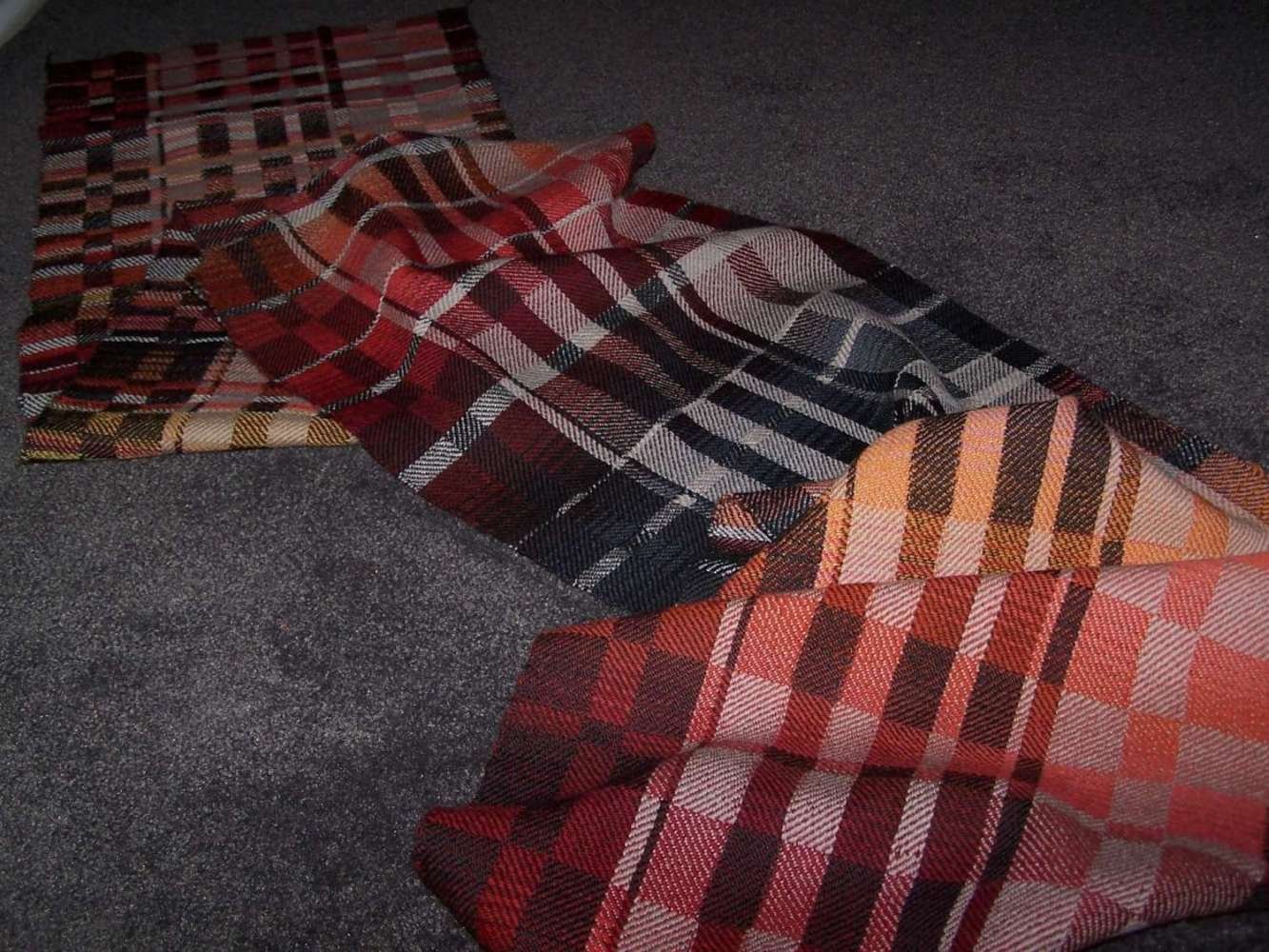 Colorful plaid blankets spread out on a dark carpeted floor.