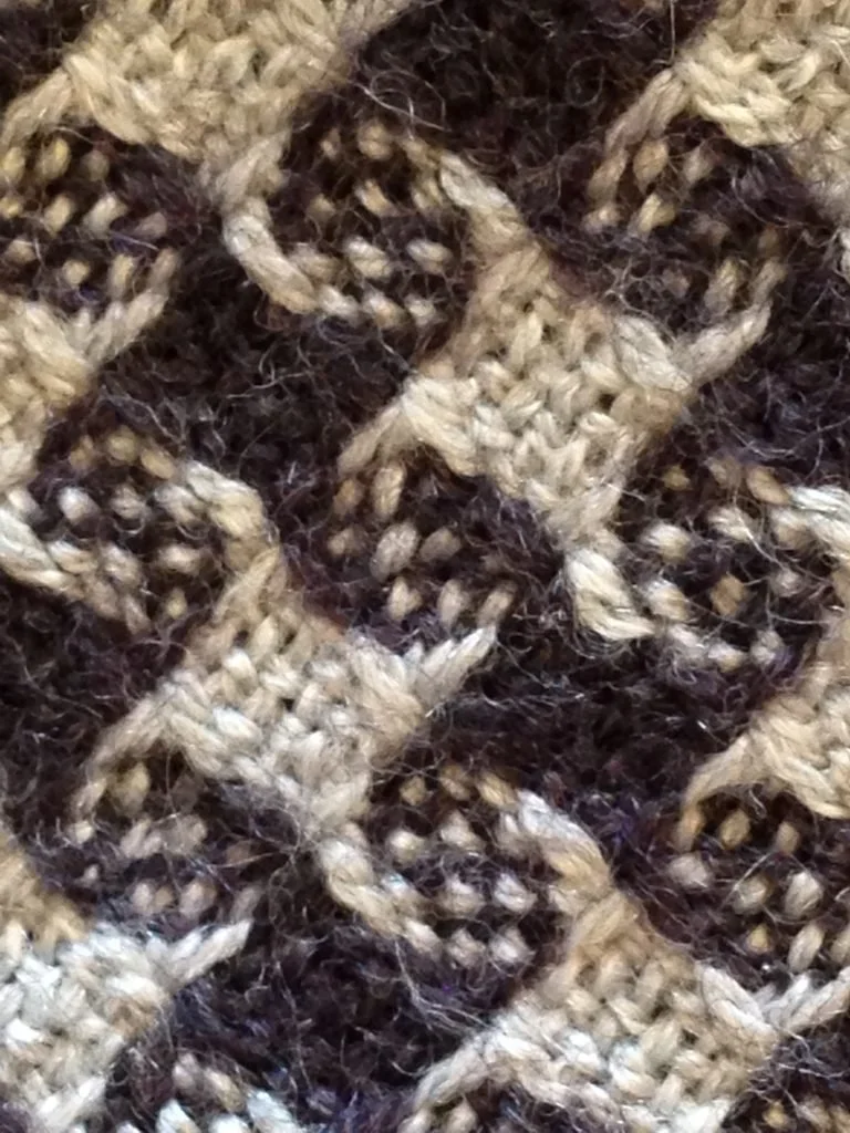 Close-up of a knitted fabric with a checkered pattern in beige and dark brown colors.