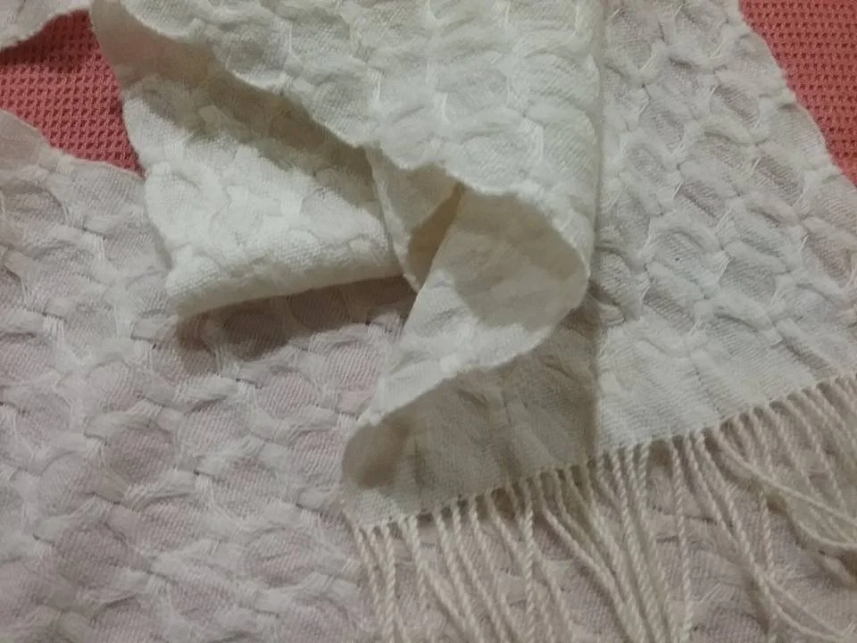 Close-up of a white textured towel with fringes on one side, draped over a pinkish woven surface.