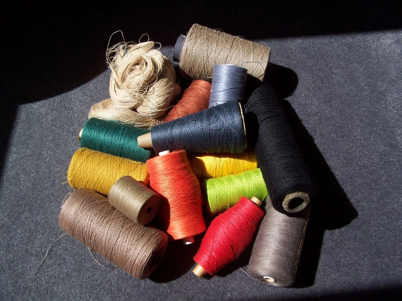 Colorful spools of thread on a dark surface, with sunlight casting shadows.