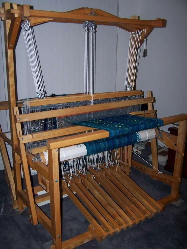 A large wooden loom used for weaving fabric or textile projects in a room with gray walls.