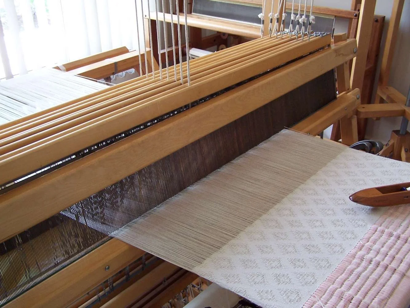 Loom weaving fabric with beige and pink patterns in a room with natural light.